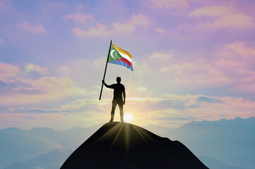 Waving flag of Comoros at the top of a mountain summit against sunset or sunrise. Comoros flag for Independence Day.