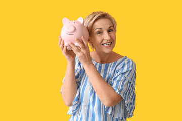 Canvas Print - Beautiful mature woman with pink piggy bank on yellow background