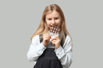 Wall Mural - Cute little girl eating sweet chocolate bar on grey background