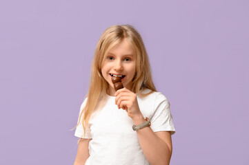 Wall Mural - Cute little girl eating sweet chocolate on lilac background