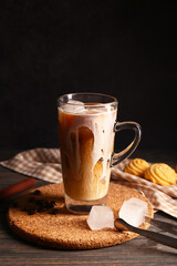 Wall Mural - Glass cup of iced latte with coffee beans and sweet cookies on wooden table