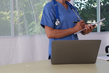 A middle-aged Asian female doctor and nurse work at a desk, providing medical advice through online consultation or tele-consultation services.