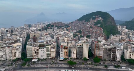 Canvas Print - Flying slowly backwards above Copacabana Beach and buildings by Avenida Atlantica, famous seaside road in Rio de Janeiro. Light fog above mountains on the horizon