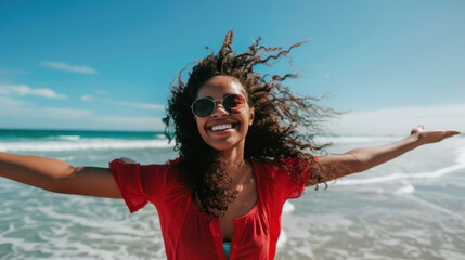 Wall Mural - a woman smiling with her arms outstretched on a beach, wearing a red shirt and sunglasses