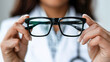 © Kowit - Professional Female Doctor Holding Black Glasses in White Coat Close Up on Light Background