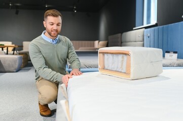 Sticker - Handsome man examining sample of orthopedic mattress on sale