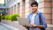 © Elathi - A young Indian male student with a laptop and backpack standing outdoors in a modern campus setting