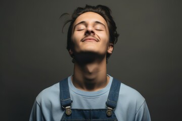 Wall Mural - young man with eyes closed wearing denim overalls over gray background