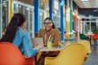 © alisaaa - Two female teachers sitting at a table, having a discussion in the lobby area in the school they work at in Gateshead, North East England. They are talking about school issues together while using a l
