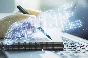 Wall Mural - creative code word hologram and hand writing in notepad on background with laptop, artificial intell