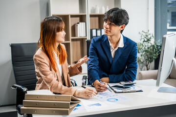 Wall Mural -  A businessman and businesswoman work late in the office, discussing strategies at a desk. They use technology and teamwork to plan and achieve success, demonstrating effective communication.