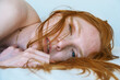 © ullision - sexy red-haired woman lies her side, close-up, her hair partially covering her face, blue eyes gaze softly, creating an intimate and serene atmosphere