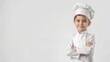 © bajita111122 - Young boy chef wearing a white uniform and hat, standing with arms crossed and smiling confidently against a plain background.