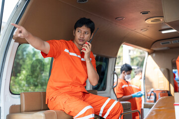 Asian male EMS paramedics or emergency medical technicians in orange uniforms talking portable radio while sitting in ambulance outside