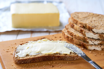 Wall Mural - knife spreading butter on rye bread slices on a white wooden table.