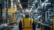 © Adi - An industrial worker in a safety vest and helmet supervises the operations in a large, complex manufacturing plant