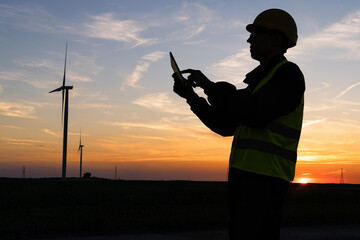 Aufkleber - Engineer with digital tablet works on a field of wind turbines at sunset	