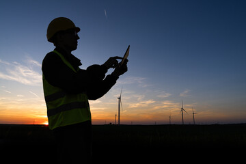 Aufkleber - Engineer with digital tablet works on a field of wind turbines at sunset	