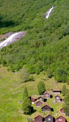 Wall Mural - Breathtaking aerial view of serene mountain cabins next to picturesque waterfalls and lush green nature. Lovatnet, Norway