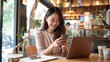 © AlfaSmart - Asian woman is sitting in a cozy modern caf using her smartphone for a video conference call