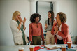 © La Famiglia - Four happy smart businesswomen around the desk while celebrating a victory in the coworking space in the office