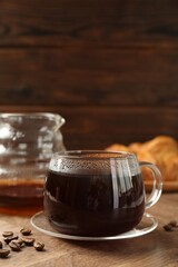 Poster - Hot coffee in glass cup and beans on wooden table, closeup. Space for text