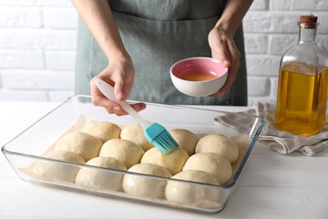 Wall Mural - Woman spreading egg yolk onto raw dough balls at white wooden table, closeup