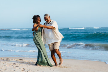 Wall Mural - Senior African American couple dancing on the beach at sunset