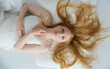 © ullision - woman with long red hair lies on a white bed, wearing a delicate lace dress. Her serene expression and soft lighting create a peaceful and dreamy atmosphere