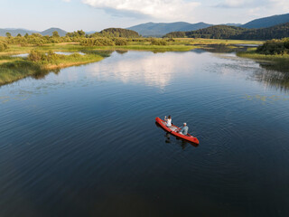 Beautiful mountain lake scenery with two people enjoying recreation paddling a red canoe, aerial shot. Summer vacation concept.