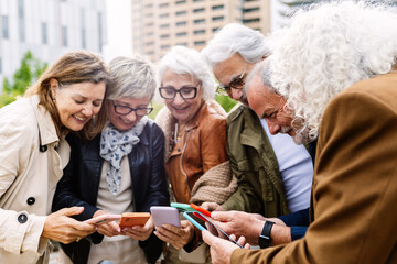 Senior group of people using mobile phone device standing in circle outdoors. Technology and baby boomers lifestyle concept