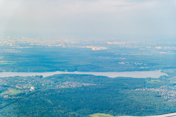 View of airplane wing, blue skies and green land during landing. Airplane window view.