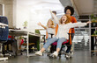 © Prostock-studio - Time for fun. Young cheerful business people racing on office chairs and laughing, free space