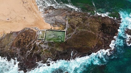 Drone shot aerial view at a beach of a beach rock pool in summer 