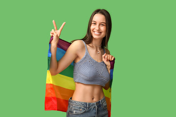 Wall Mural - Beautiful young happy woman with piercing navel and LGBT flag showing victory gesture on green background