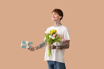 Wall Mural - Young tattooed man with gift and tulips on beige background. International Women's Day celebration