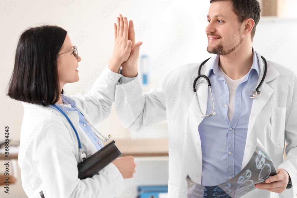 Doctors with x-ray images giving each other high-five in clinic