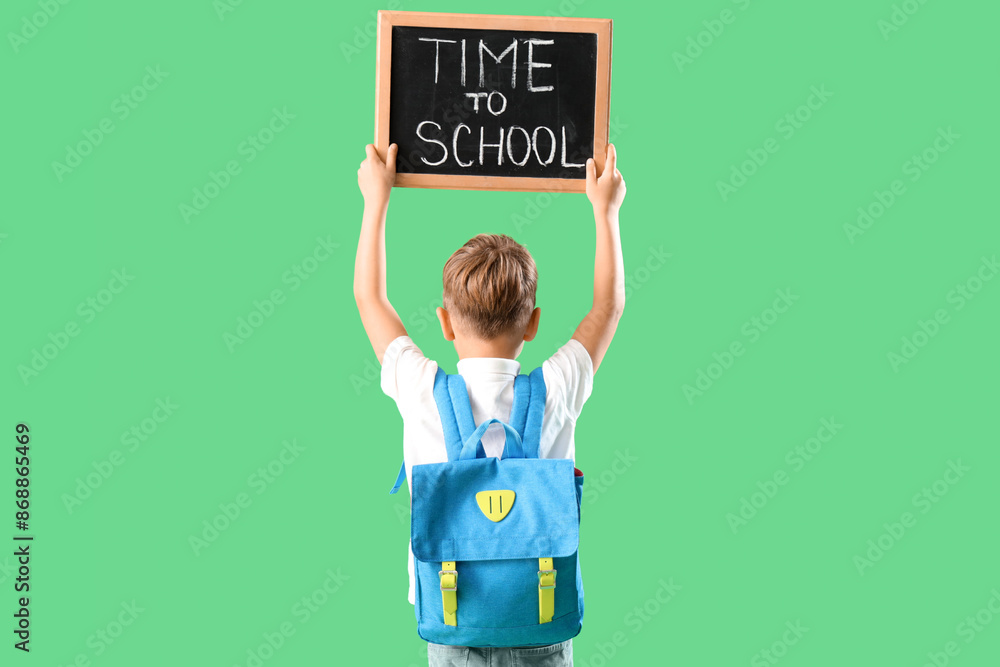 Little boy holding chalkboard with text TIME TO SCHOOL on green background, back view