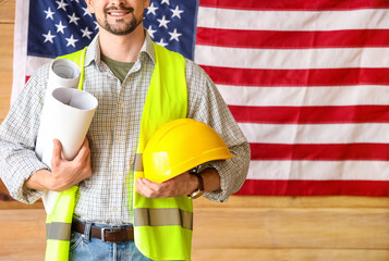 Wall Mural - Male architect with house plans and hardhat against USA flag in workshop. Labour Day celebration