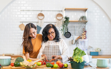 Wall Mural - Portrait of happy love asian family senior mature mother and young daughter smiling cooking vegan food healthy eat with fresh vegetable salad and fruit in kitchen, care, insurance, elderly health care