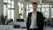 © Abelorz - A confident young man in business attire stands proudly at the front of an open office space, exuding confidence and success as he does. Daylight coming through large windows in the background.