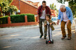 © Geber86 - Father and grandfather teaching young boy to ride a scooter on suburban street