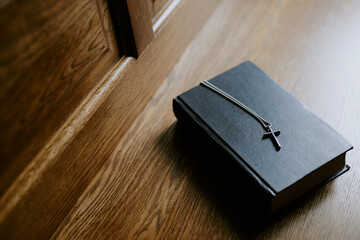 High angle view closeup of Holy Bible book with silver cross on wooden pew in Catholic church