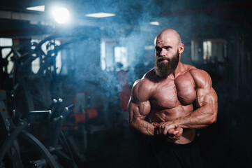 Wall Mural - Muscular bald man posing shirtless. Bodybuilder showing off his shape in the gym. 