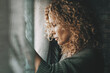 © simona - Sadness worried woman inside home near the window. Bad unhappy day. Side view of female people sad with depression. Problems and home domestic loneliness. House couple violence. Wife alone in trouble