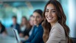 © Robert Anto - A smiling businesswoman in a beige blazer seated at a conference table, engaging with colleagues in a modern office, showcasing teamwork and professionalism.