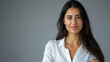 © PrabhjitSingh - Portrait of a smiling businesswoman with Middle Eastern features, and long dark hair, standing with arms crossed against a light grey background
