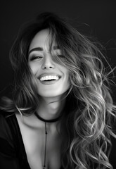 Beautiful young woman in her late 20s, smiling with long wavy hair in a high contrast black and white photograph. Timeless and elegant portrait