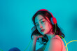 © dashstudio - Portrait of beautiful young korean girl listening to music in headphones against blue studio background in neon light