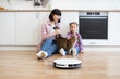 © sofiko14 - Mother and daughter playing with cat on kitchen floor while robotic vacuum cleaner operates. Modern home setting showing interaction with pet cats and use of smart home technology.